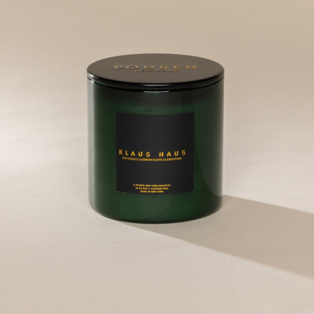A dark green glass jar candle with a black lid and a black label featuring gold lettering that reads &