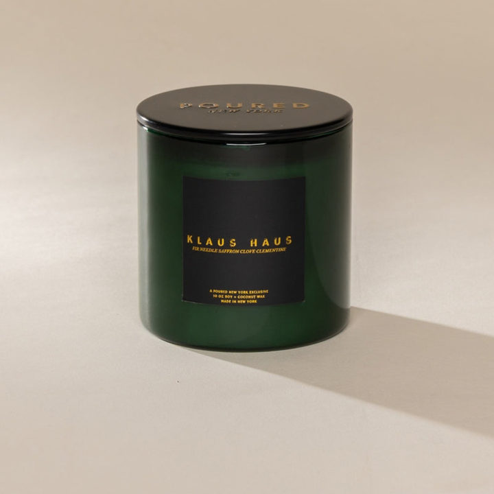 A dark green glass jar candle with a black lid and a black label featuring gold lettering that reads &
