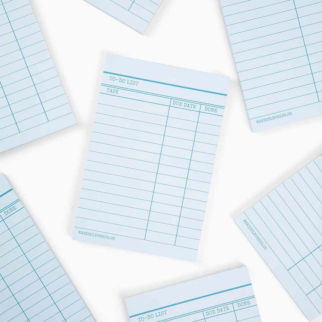 Light blue lined notepad pages with a to-do list table layout, arranged in a flat-lay pattern on a white background.