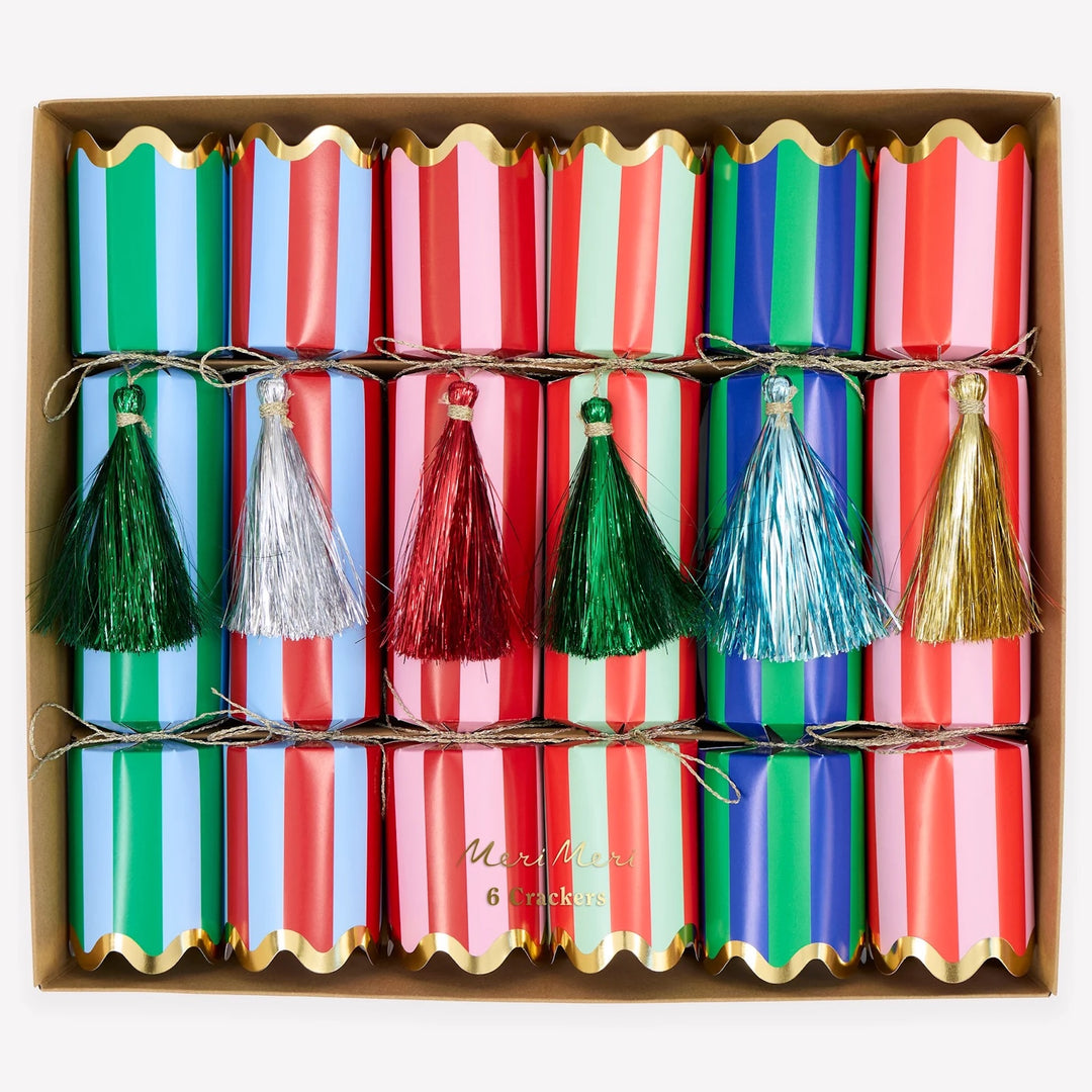 A boxed set of six Christmas paper cracker fireworks with colorful striped wrappers in green, blue, pink, and red, decorated with metallic tassel pulls in green, silver, red, blue, and gold.