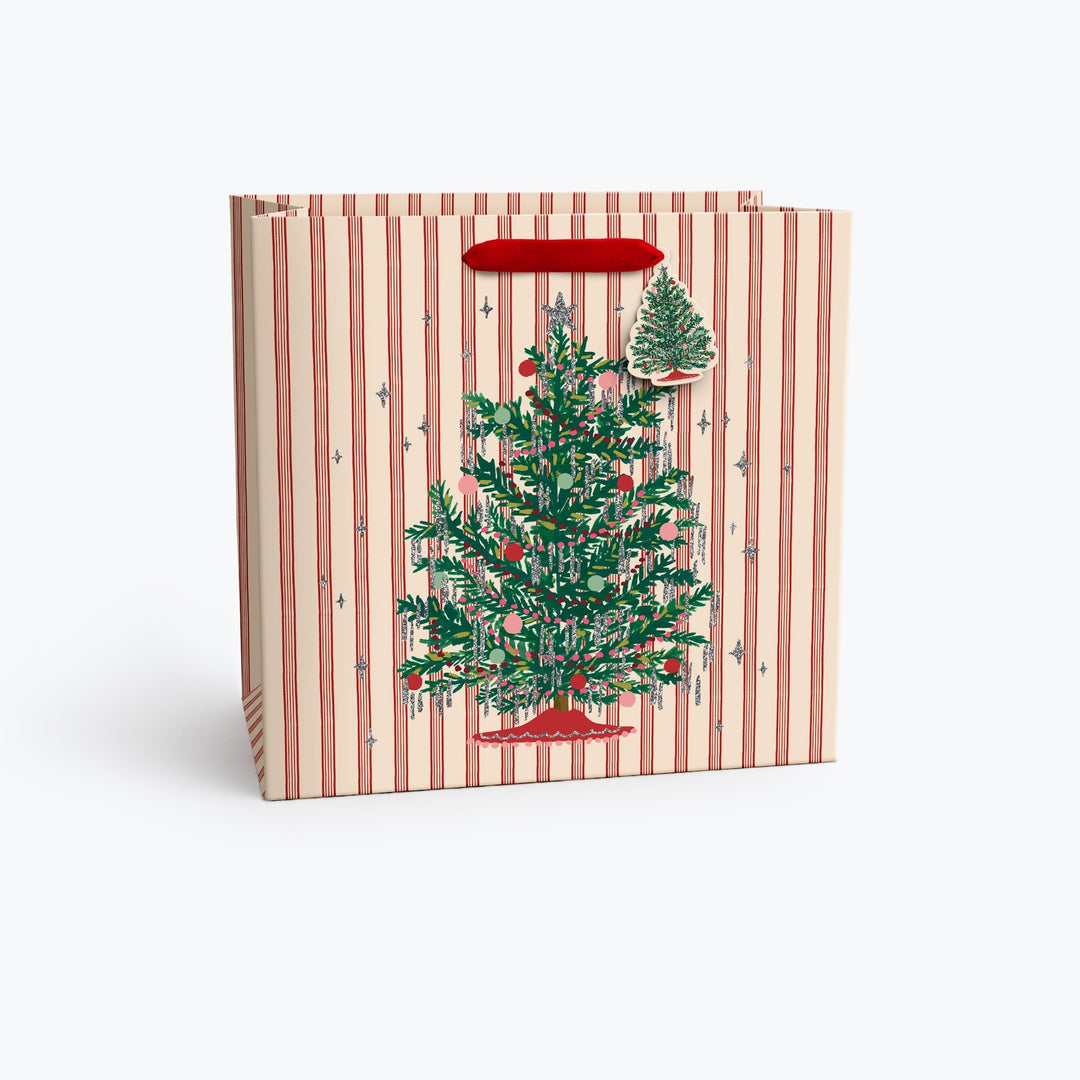 A gift bag with a festive Christmas design, featuring a red and cream striped pattern, a large green Christmas tree illustration, a smaller tree sticker, and a red handle, shown on a clean white background.