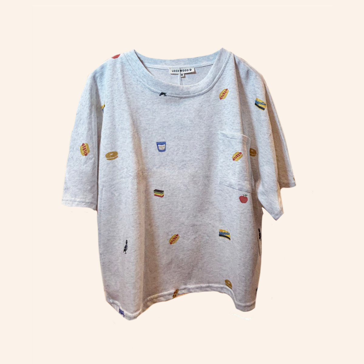 A light gray heather short-sleeve t-shirt with a small multicolor food-themed print scattered across the front, featuring a chest pocket and a visible 'sunday girls' brand label inside the collar.