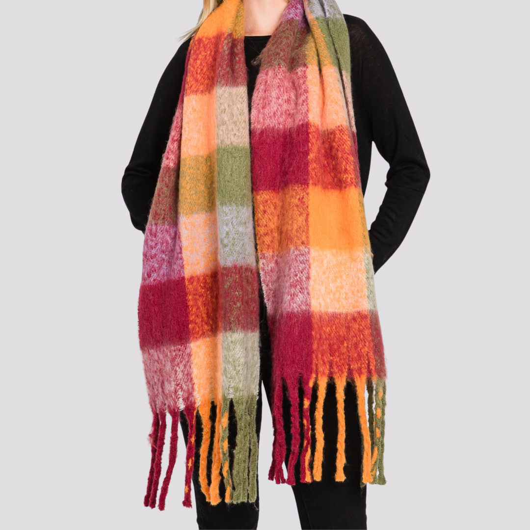 A person wearing a long, fuzzy plaid scarf in warm autumn colors including orange, pink, red, yellow, and green, paired with a black top against a light gray background.