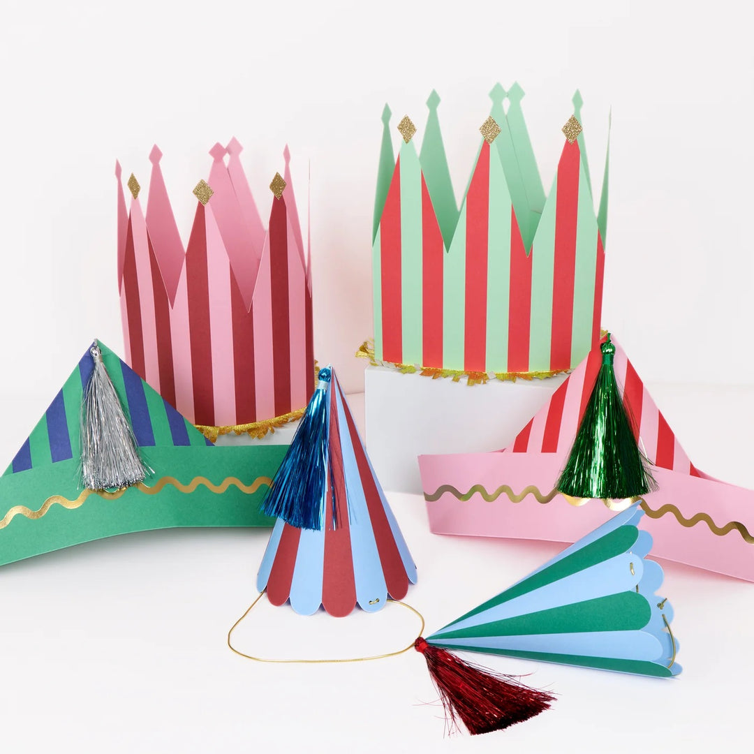A set of colorful paper party hats and crowns with red, green, pink, and blue stripes, decorated with metallic gold trim and tassels, displayed on a clean white background.