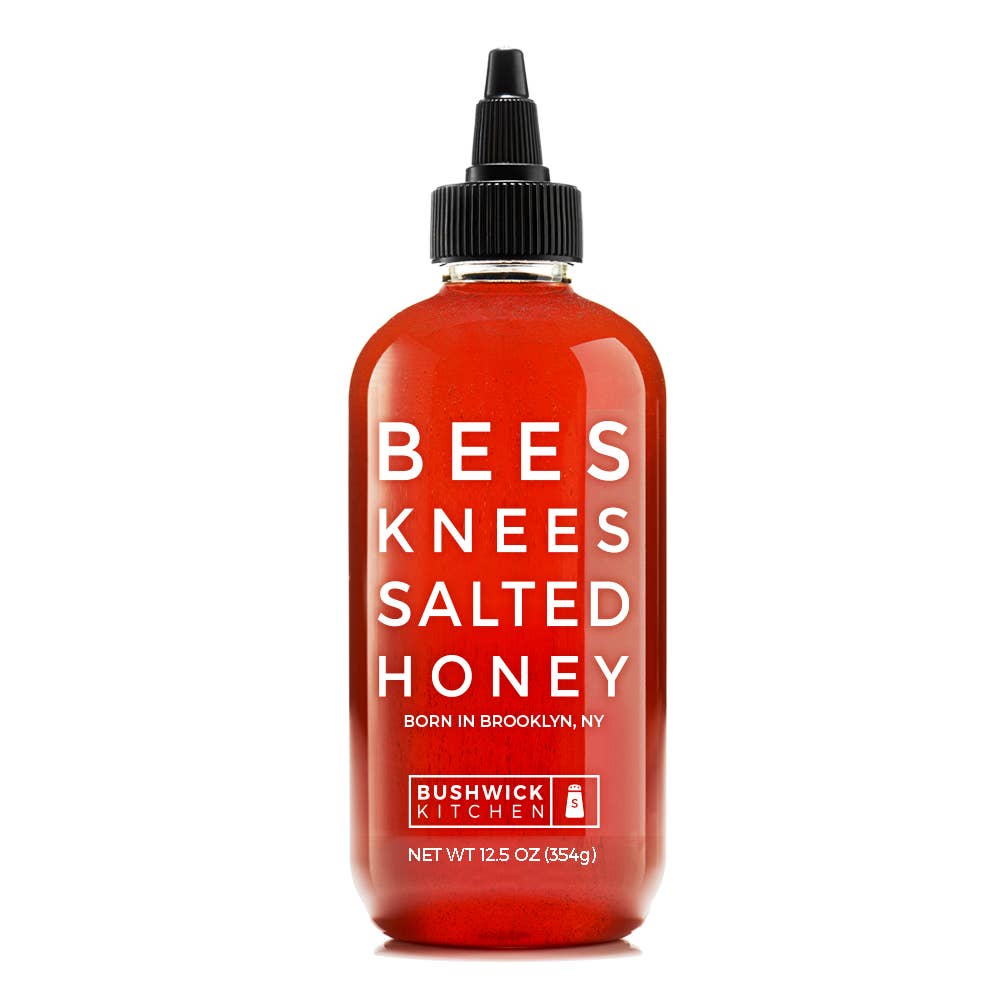 A bottle of Bushwick Kitchen Bees Knees Salted Honey, featuring a translucent red bottle and a black squeeze cap, on a solid white background.