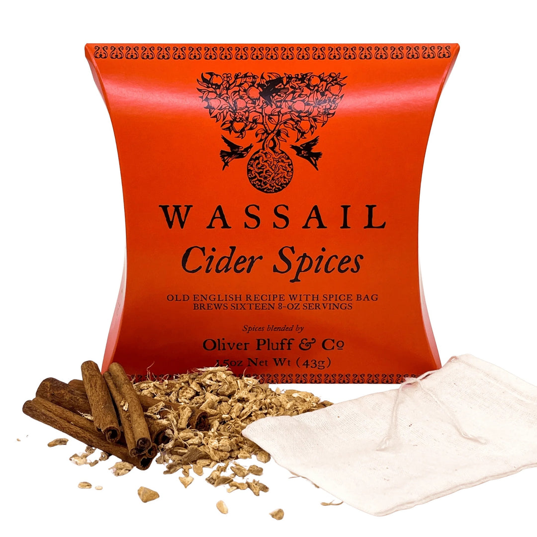 Wassail Cider Spices by Oliver Pluff &amp; Co, featuring a bright orange-red pouch with black text and a decorative tree of life logo, displayed with cinnamon sticks, loose spices, and a cloth bag on a white background.