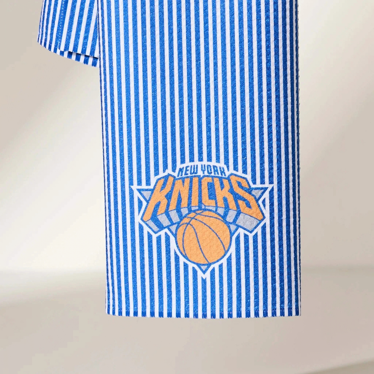 A close-up of a blue and white vertically striped fabric item featuring the New York Knicks logo in the center.