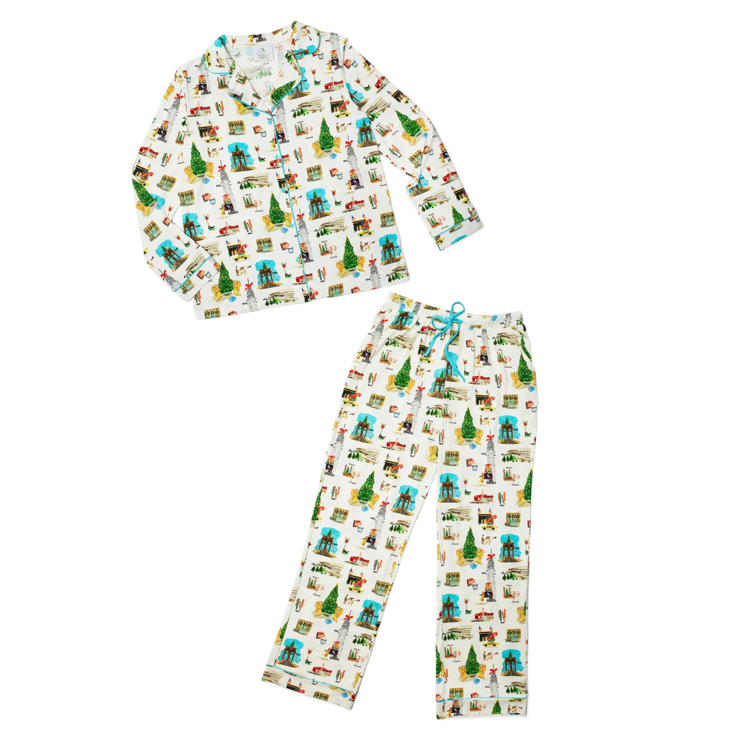 A two-piece long-sleeve pajama set featuring a matching top and pants with an all-over whimsical cartoon print on a white background. The print includes small green trees, blue birds, red houses, and other colorful illustrations.