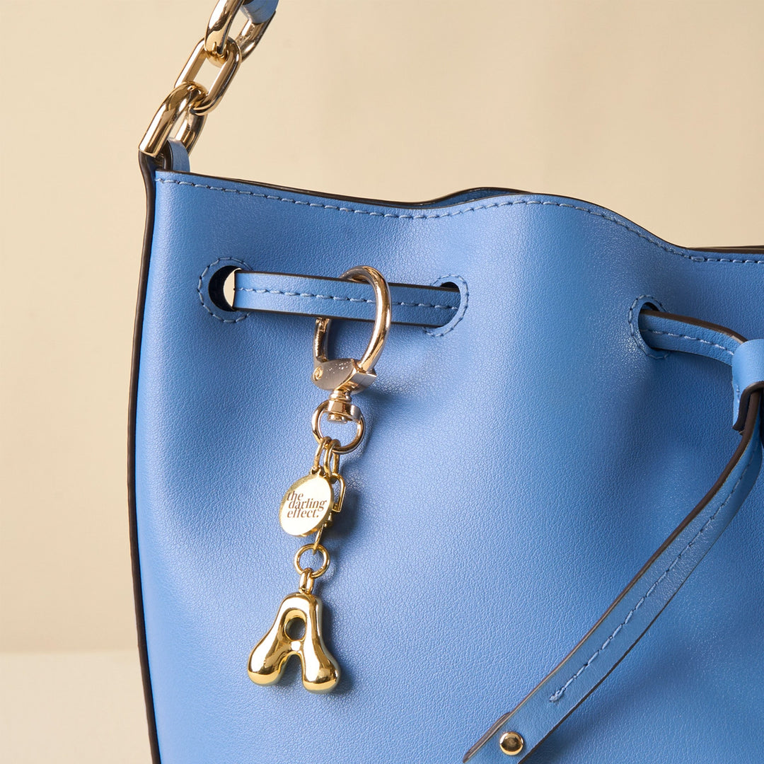 a blue handbag with a gold a shaped bag charm on it