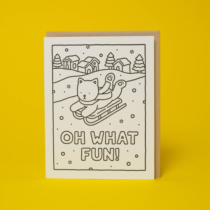 A white greeting card with a black line drawing of a cat in a sled in a snowy winter scene, with the text &