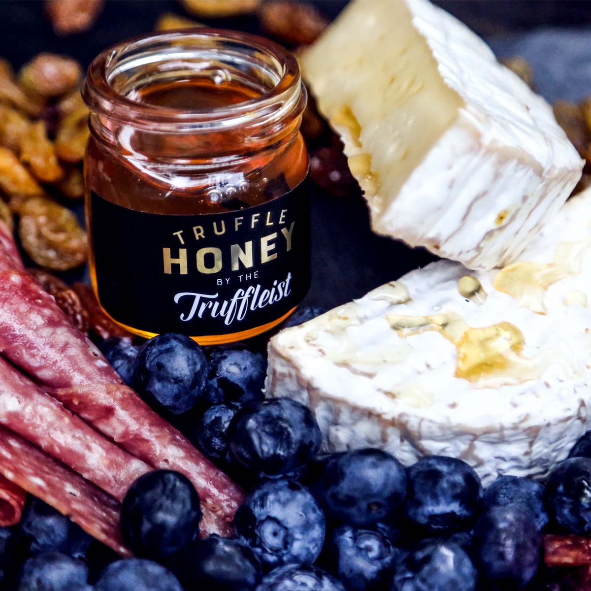 Jar of truffle honey with cheese and berries on a platter.