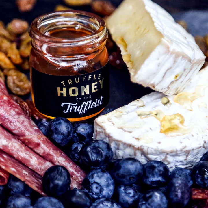 Jar of truffle honey with cheese and berries on a platter.