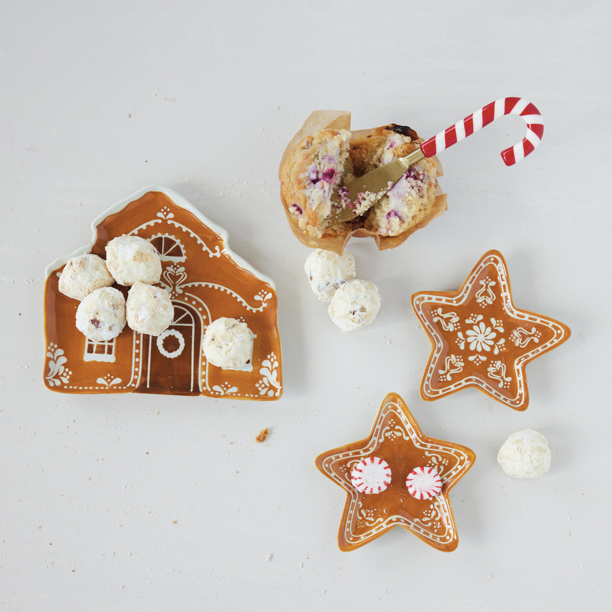 Decorative gingerbread cookies shaped like a house and stars with white and red candies on a light background.