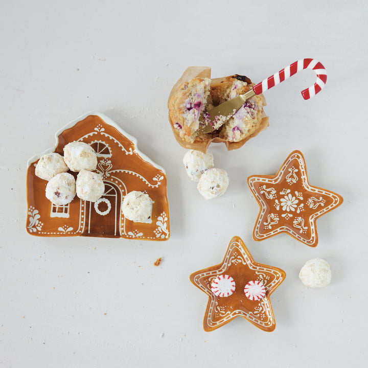 Decorative gingerbread cookies shaped like a house and stars with white and red candies on a light background.