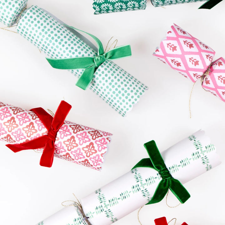 Several Christmas cracker ornaments wrapped in festive patterned paper and tied with satin ribbons, arranged on a clean white background.