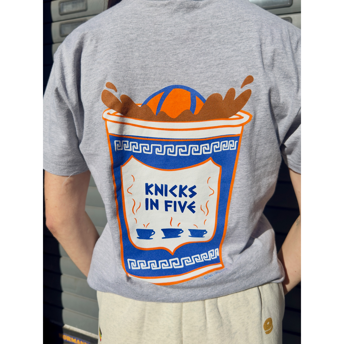 Back of t shirt that features the same image of the anthora cup reading "Knicks in Five" but closer up and the basketball being dunked.