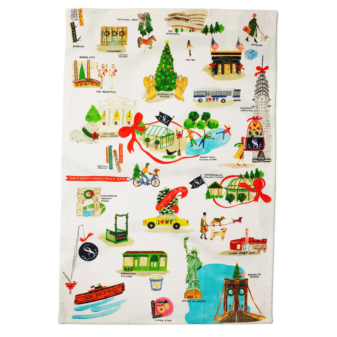 An off-white cotton tea towel featuring a colorful illustrated collage of New York City landmarks and scenes, including the Statue of Liberty, Empire State Building, Brooklyn Bridge, Times Square, and a Christmas tree.
