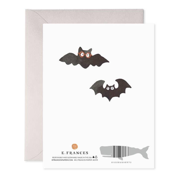 A white greeting card with two black bat illustrations and a gray envelope behind it, photographed on a clean white background. The card shows the brand name E.