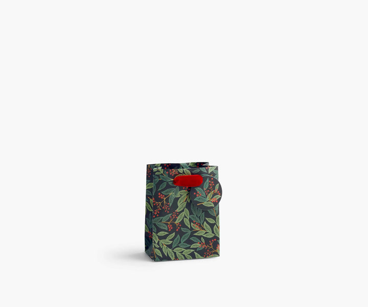 A small paper gift bag with a dark green and black botanical leaf pattern and a bright red ribbon handle, set against a plain white background.