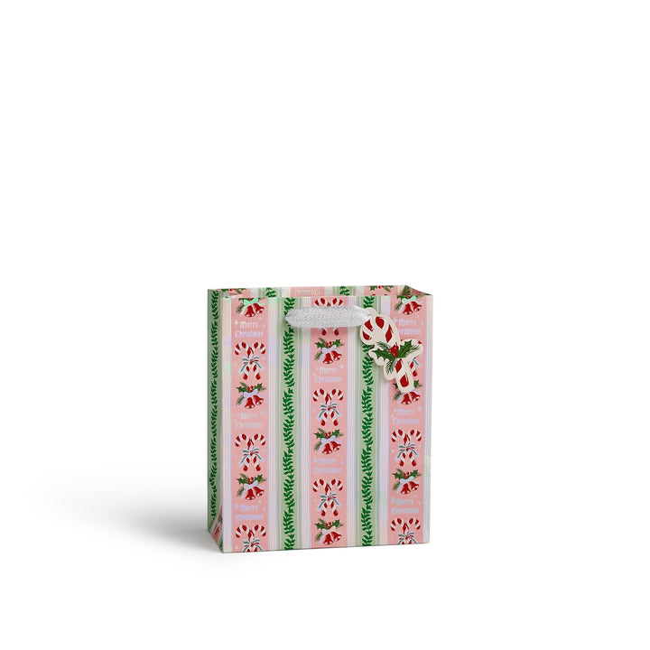 A small gift bag with a pink and white striped pattern, decorated with green pine branches and red candy canes, featuring a white bow on the handle, set against a plain white background.