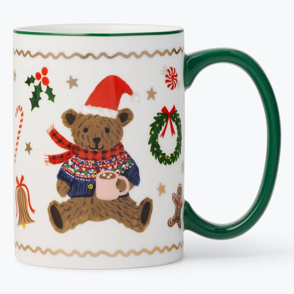 A white ceramic Christmas mug with a dark green handle and rim, decorated with a festive illustration of a teddy bear in a red Santa hat and patterned sweater, surrounded by holiday motifs like a wreath, candy cane, and gingerbread man.