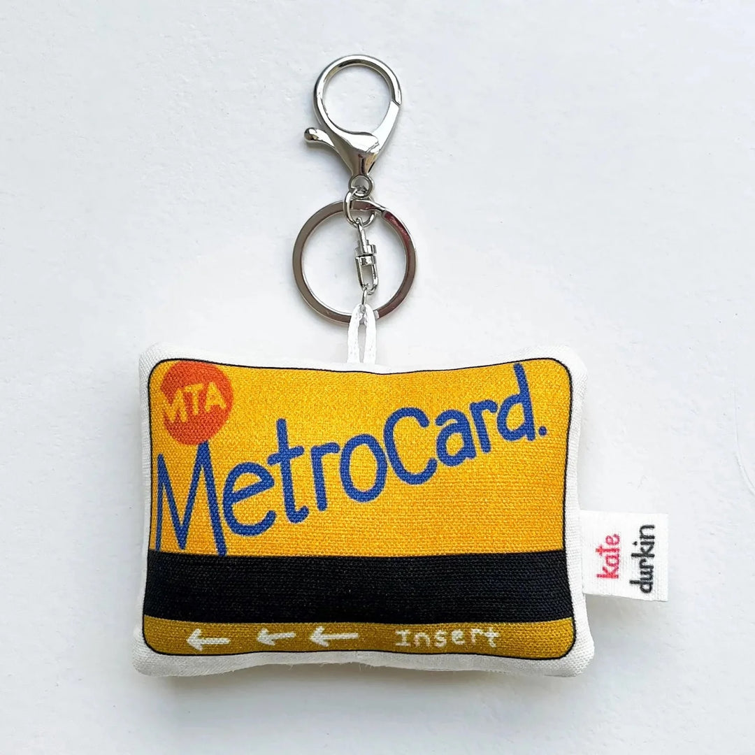 A fabric keychain designed to look like a yellow and black MetroCard with a silver metal keyring, shown on a plain white background.