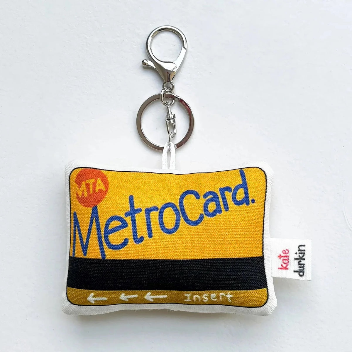 A fabric keychain designed to look like a yellow and black MetroCard with a silver metal keyring, shown on a plain white background.
