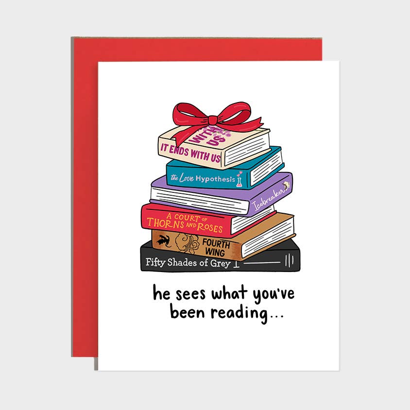 A white greeting card with a red envelope behind it, featuring an illustration of a stack of colorful books tied with a red bow and the text 'he sees what you've been reading.