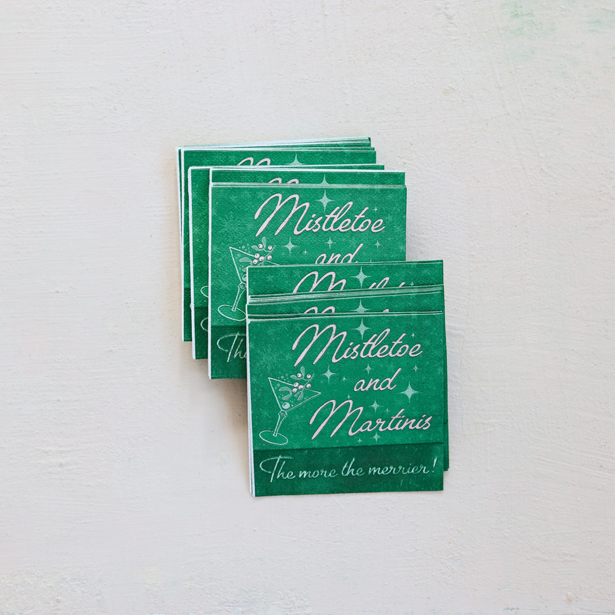A stack of green cocktail-themed cards or napkins with white script text reading 'Mistletoe and Martini' and a martini glass illustration, arranged on a light textured background.
