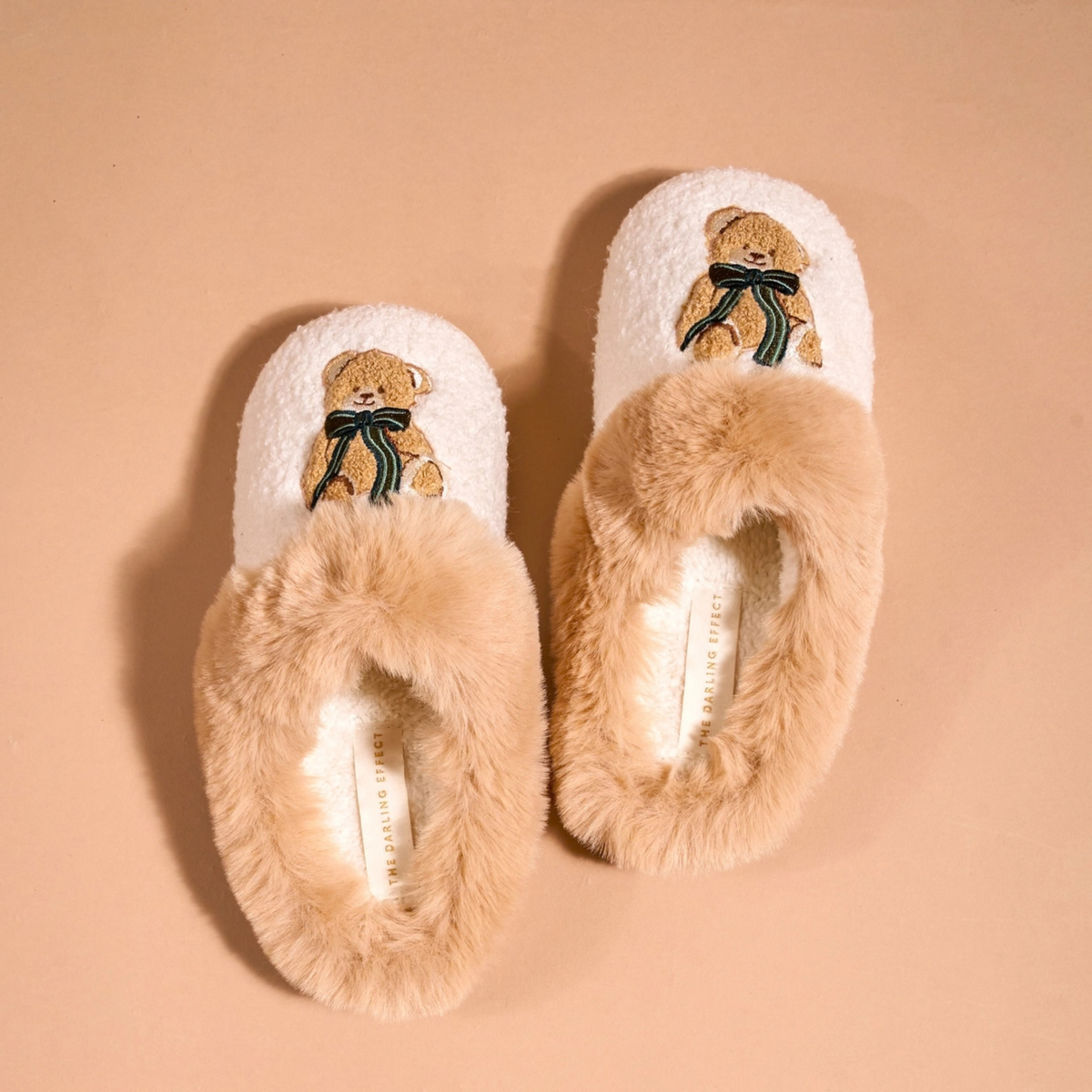Pair of fluffy slippers with teddy bear design on a beige background