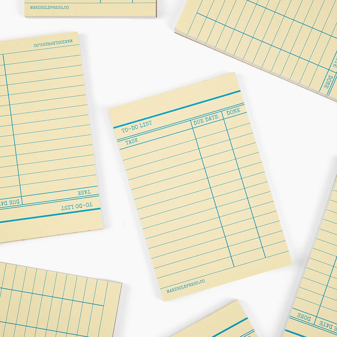 A set of cream-colored to-do list notepads with teal blue grid lines and printed text, arranged in a flat-lay pattern on a white background.