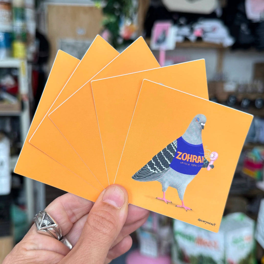 A hand holds a fan of square orange cards featuring a pigeon illustration wearing a blue shirt with the text &