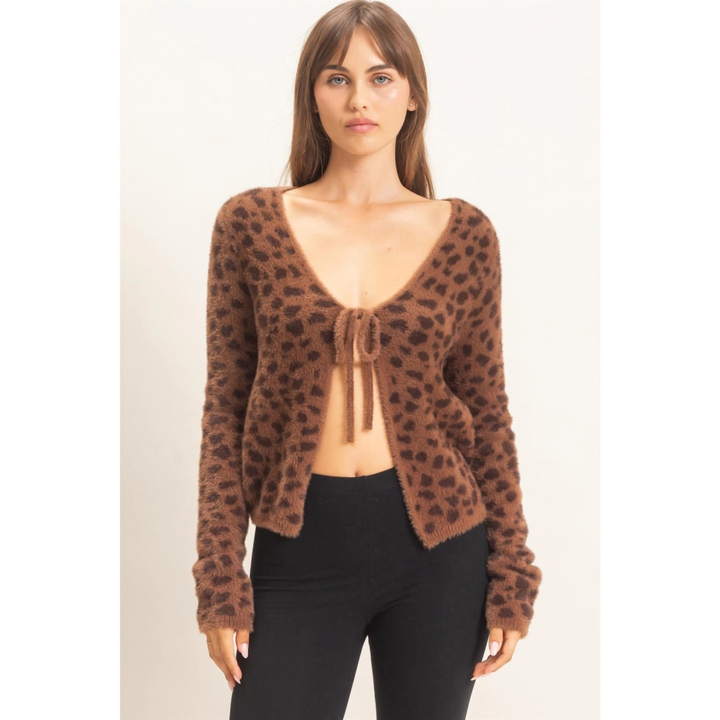 A woman modeling a brown fuzzy leopard-print cardigan with a tie-front detail and black pants, photographed against a plain light background.