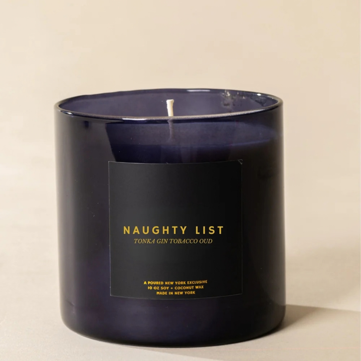 A dark navy blue glass jar candle with a black label featuring gold text that reads &