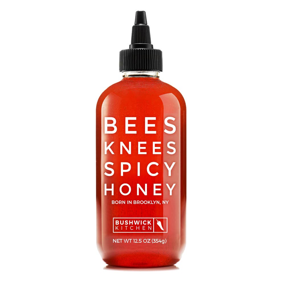A bottle of Bushwick Kitchen Bees Knees Spicy Honey, featuring a translucent red-orange liquid inside a clear bottle with a black dropper cap and white text on the front, set against a plain white background.