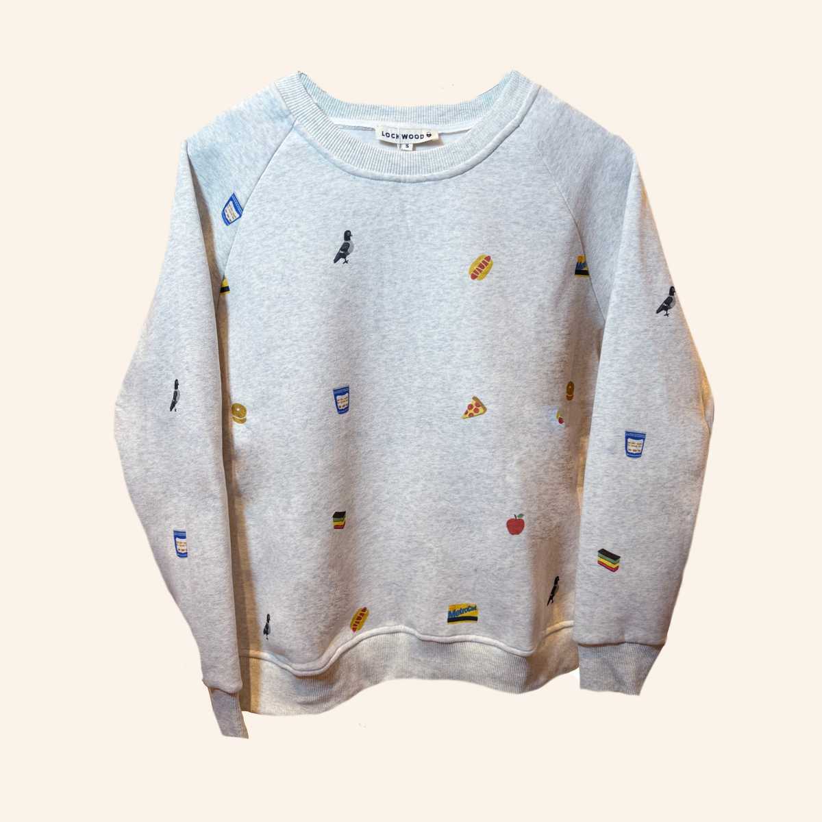 A light gray heather crewneck sweatshirt with small colorful food-themed prints, shown against a solid pale beige background. The brand name 'SWEETHEART' is visible on the inner neck label.