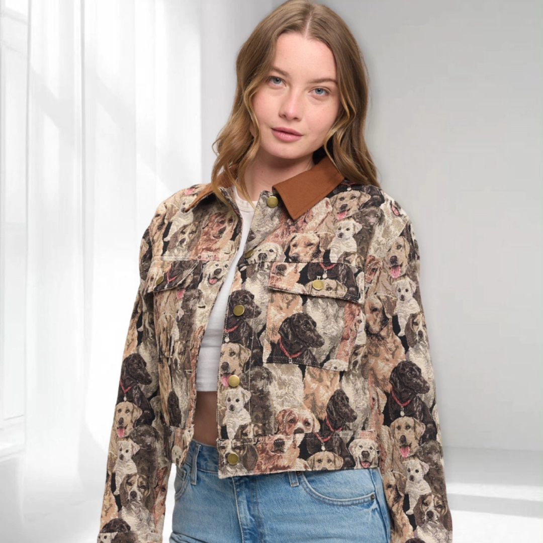 A woman wearing a cropped button-up jacket covered in a detailed print of various dog portraits, featuring a solid brown collar, styled with a white top and blue jeans.