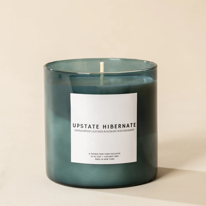 A dark teal-green glass jar candle with a white label reading &