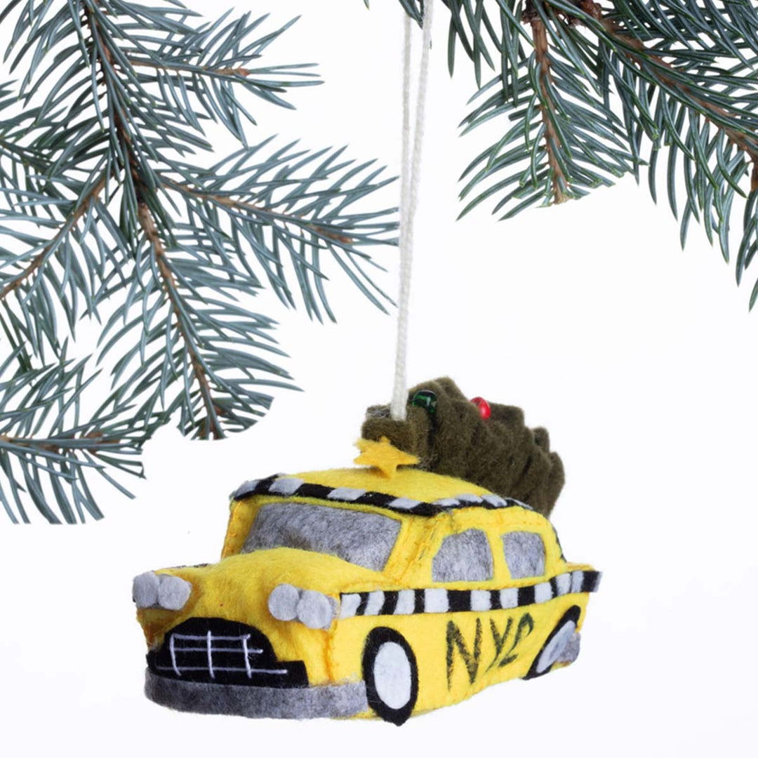 Yellow taxi Christmas ornament with a Grinch on top, hanging from a tree branch.
