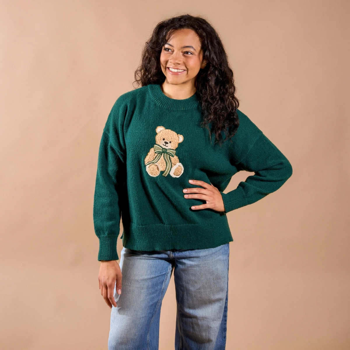 Person wearing a green sweater with a teddy bear design against a beige background