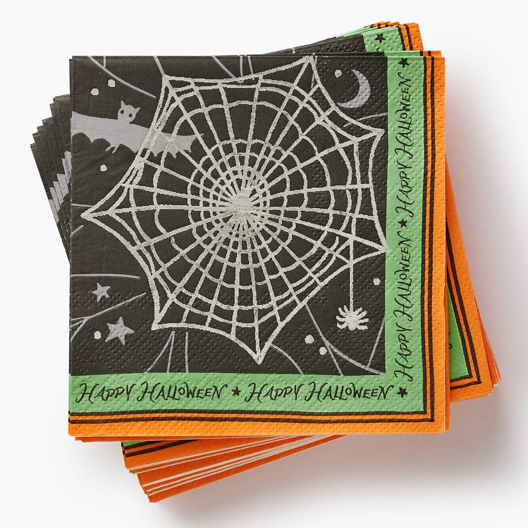A stack of Halloween-themed paper napkins featuring a large white spiderweb design on a black background, with orange and green borders and &