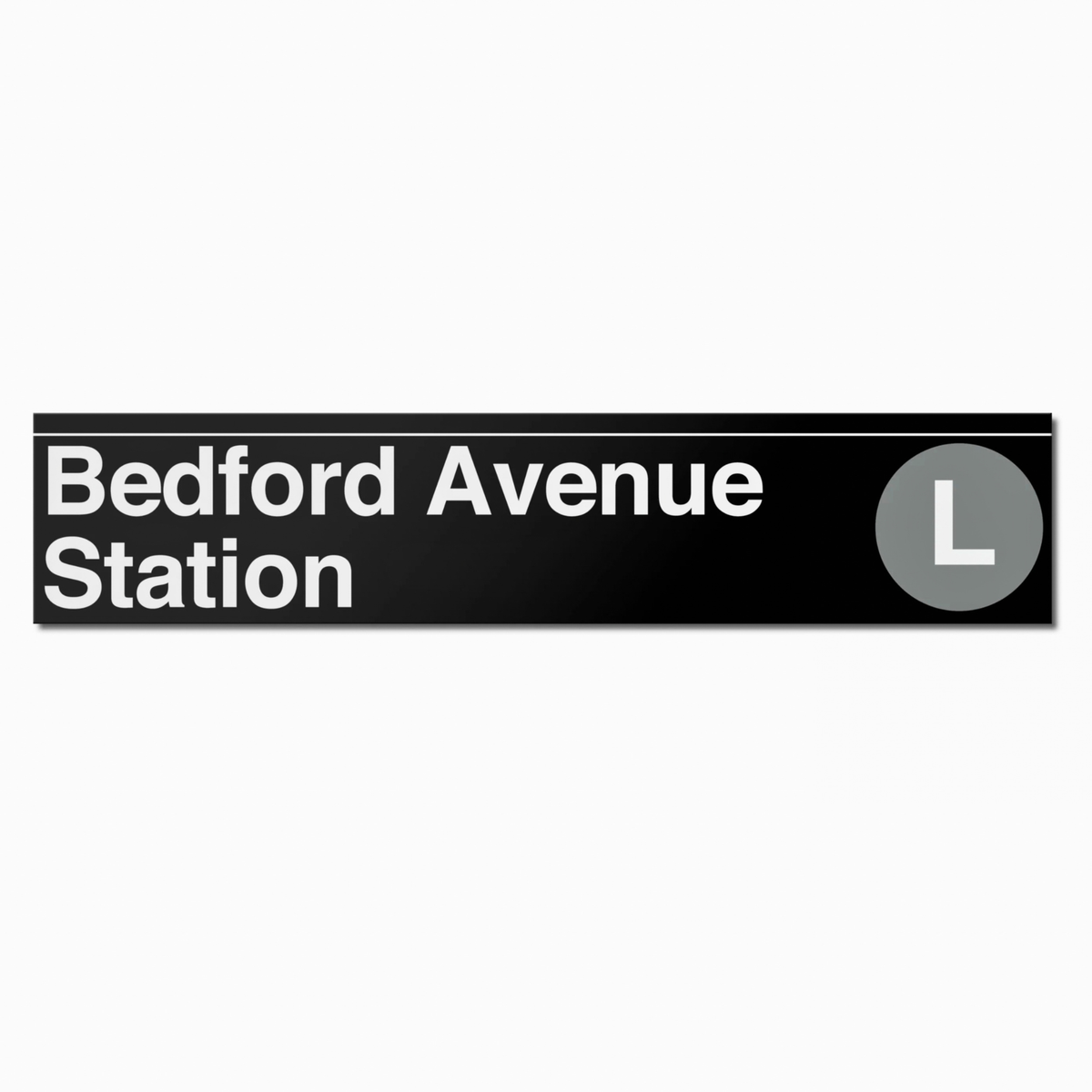 A black rectangular sign reading 'Bedford Avenue Station' in white text, with a gray circle containing the letter L on the right side, shown on a light gray background.