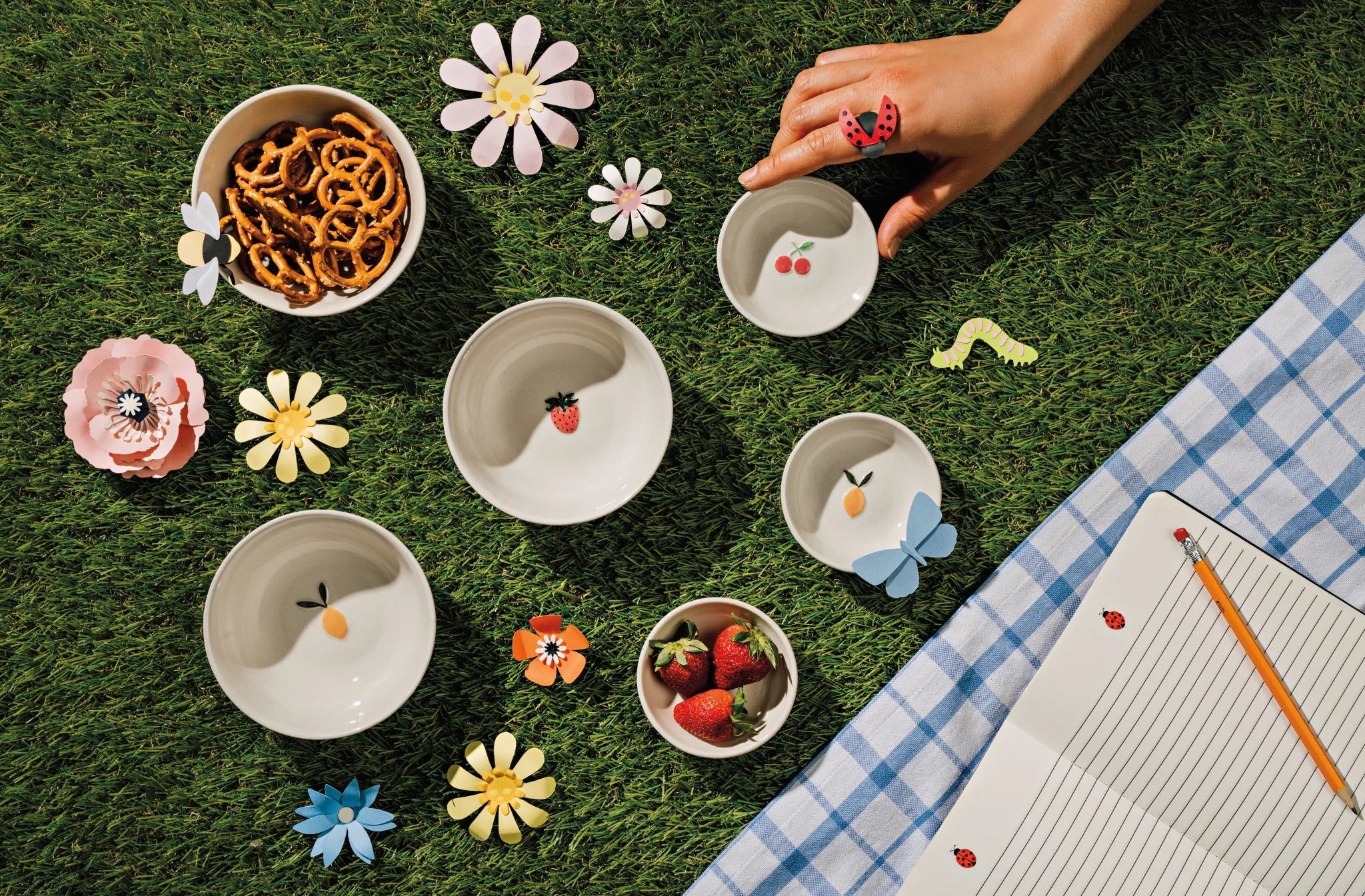Children's play area with small bowls, flowers, and a checkered blanket.