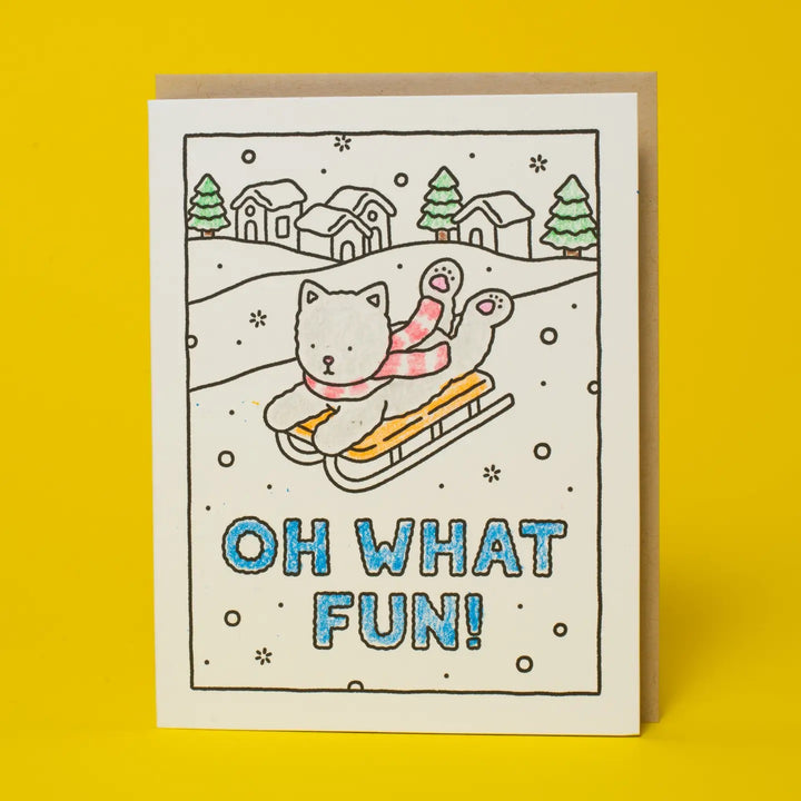A square greeting card with a hand-drawn winter scene showing two cats in sleds, with the text &